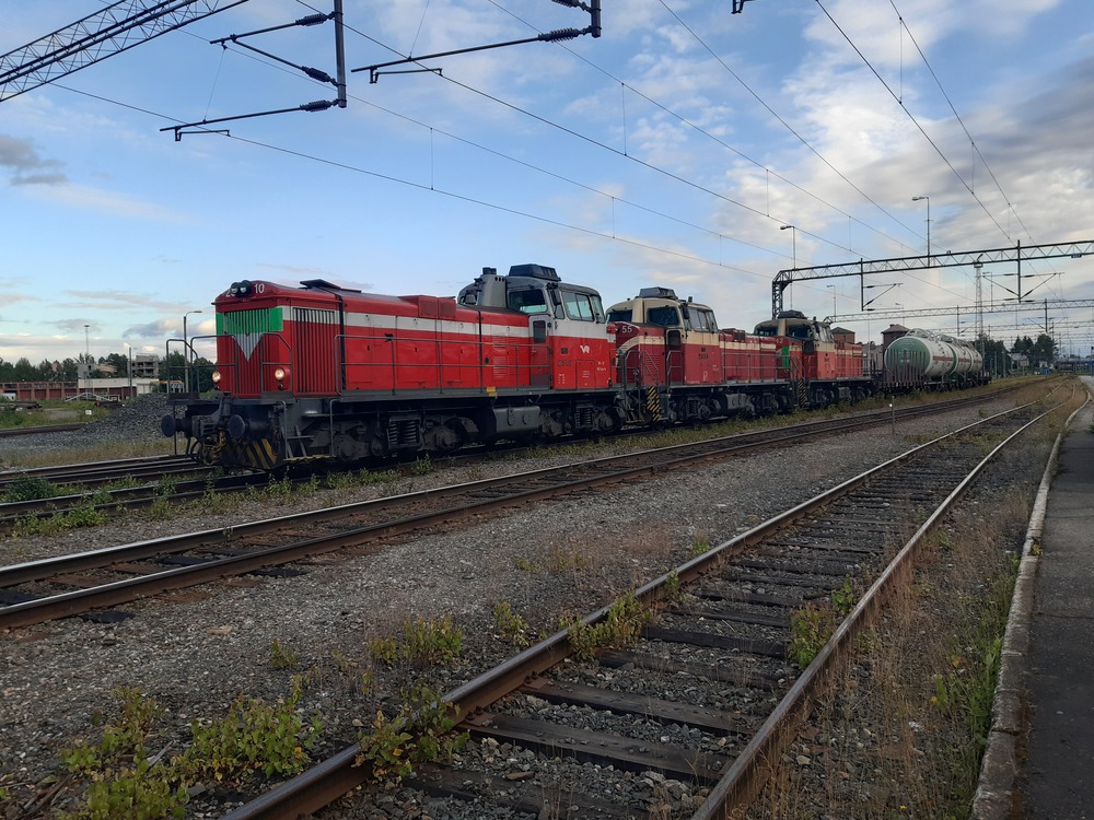 Niirala-Pieksämäki -rahti Joensuussa 24.7.2019
Iltainen Niirala-Pieksämäki sekatavarajuna toi mukavaa väriä Pieksämäki-Joensuu -radan muutoin kovin yksitotiseen ja raakapuupainotteiseen liikenteeseen. Tuona iltana T 54523 ei kuitenkaan ollut järin pitkä eikä oikein sekalainenkaan. Tripladeeveri kuljetti kolmea rajan takaa tullutta pyttyä turvavaunujen kera. Juna on pysähtynyt miehistönvaihdolle ja odottamaan lähtöaikaa, jonka jälkeen vaunujen matka jatkuu Joensuusta länteen, Kuopiosta pohjoiseen.
Avainsanat: op_VR;jt_Tavarajuna;jt_Runkojuna;jyv_Dv12;jyv_Hkba;jyv_Vgobo
